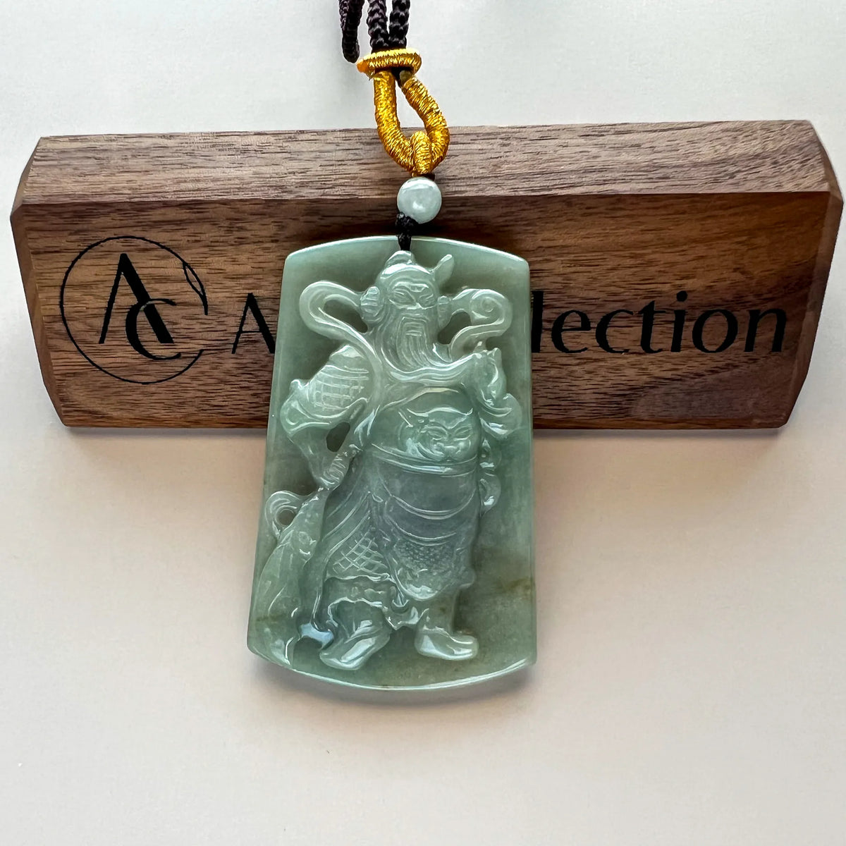 Front view of carved green jade pendant with braided cord and bead detail