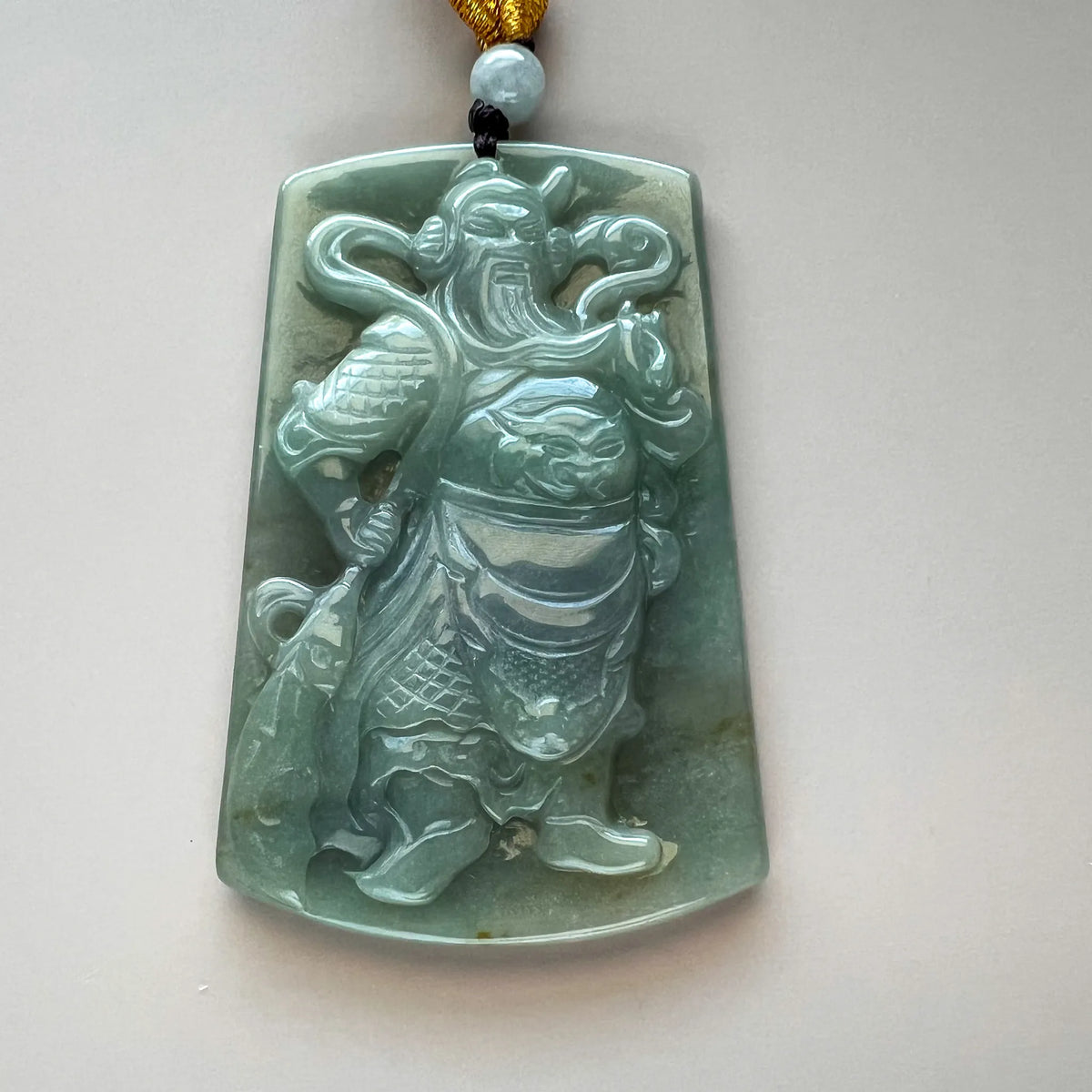 Close-up front of green jade pendant with detailed carved figure
