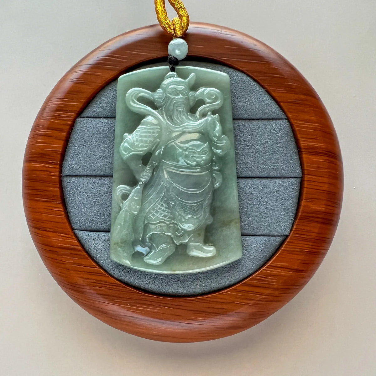 Jade pendant displayed on round wooden stand, front view with braided cord