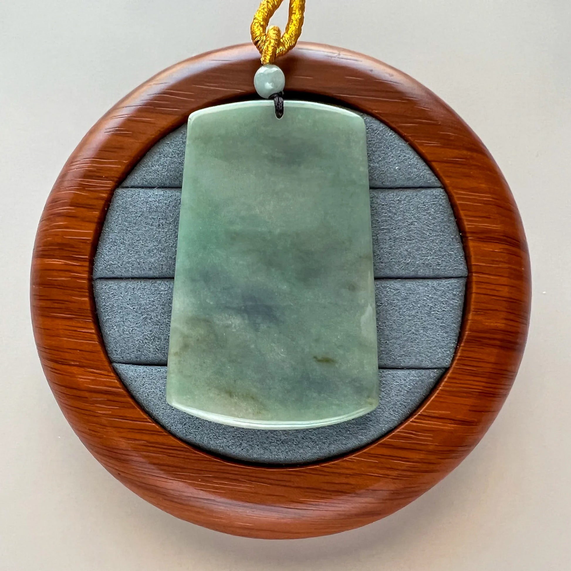 Back of the light green natural jade pendant showing a smooth polished surface, drilled hole, bead, and cord