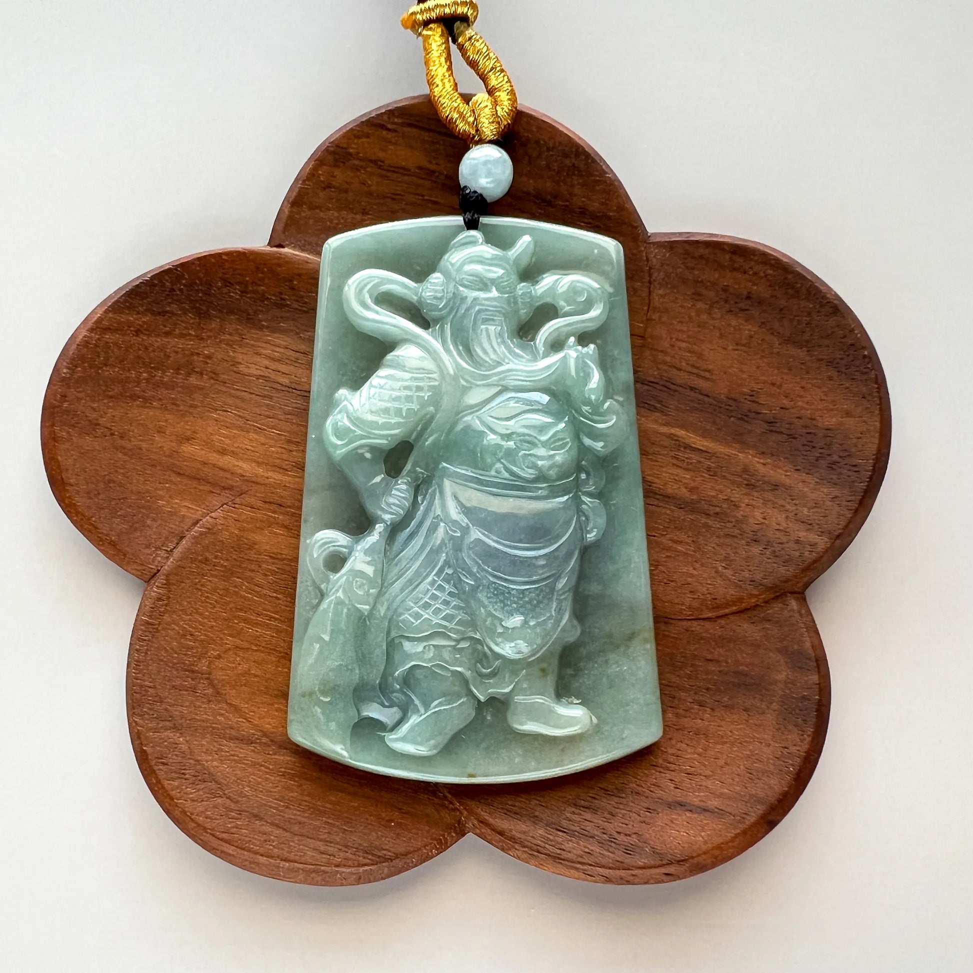 Carved jade pendant shown on flower-shaped wooden display stand, front view