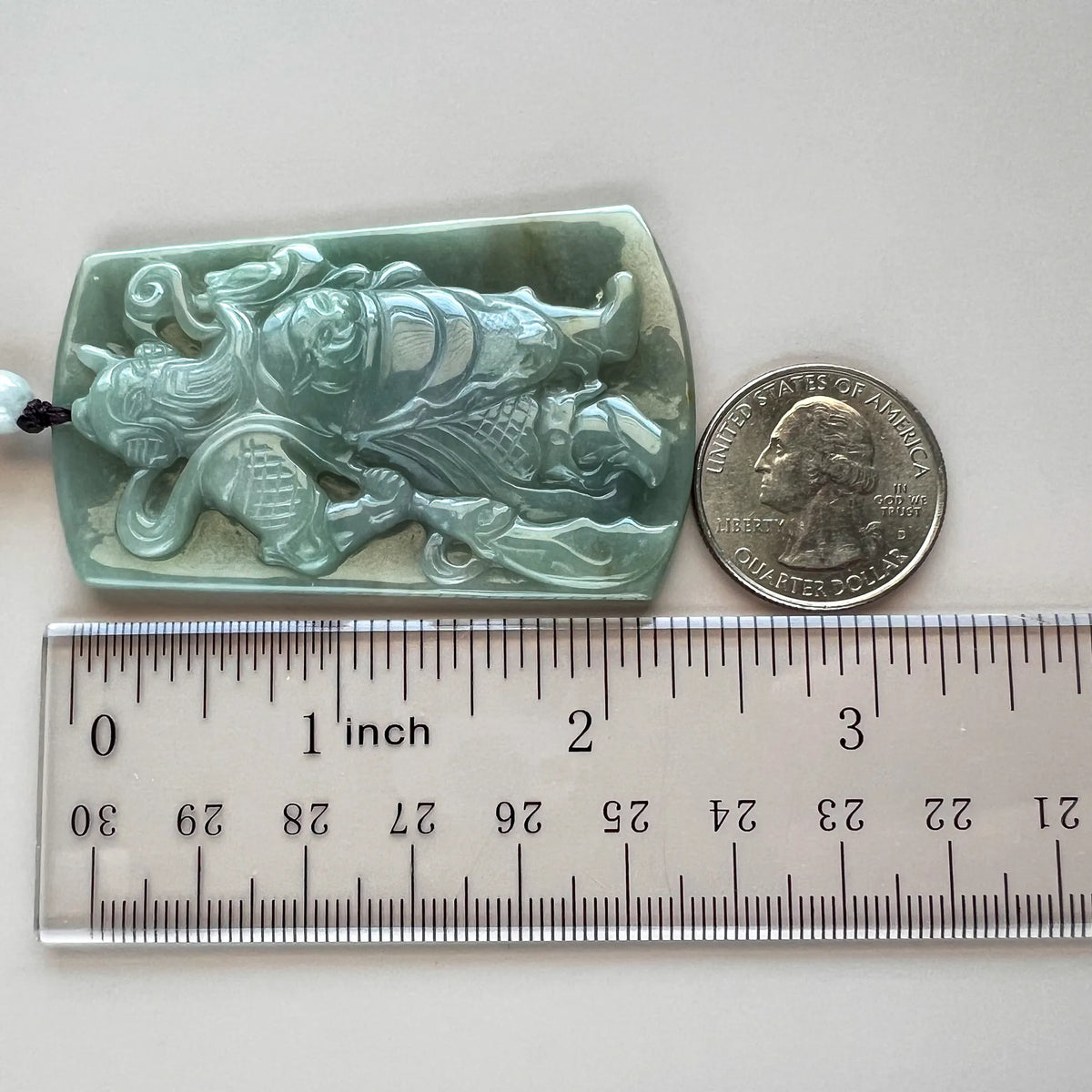 Side view of carved jade pendant with ruler and quarter for size reference