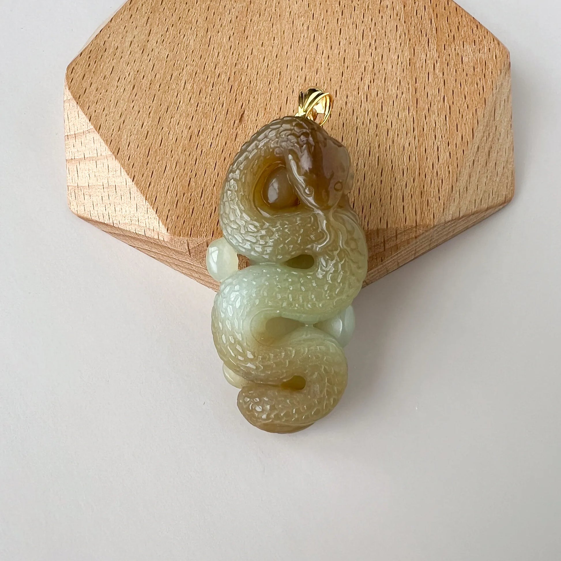 Front view of carved jade snake pendant on a wooden display block, polished gold bail visible