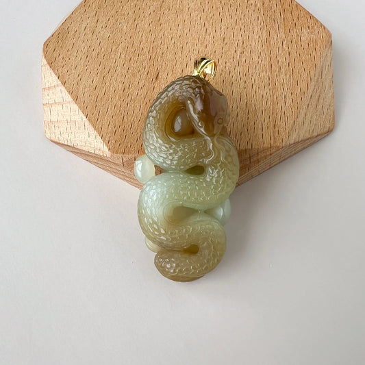 Front view of carved jade snake pendant on a wooden display block, polished gold bail visible