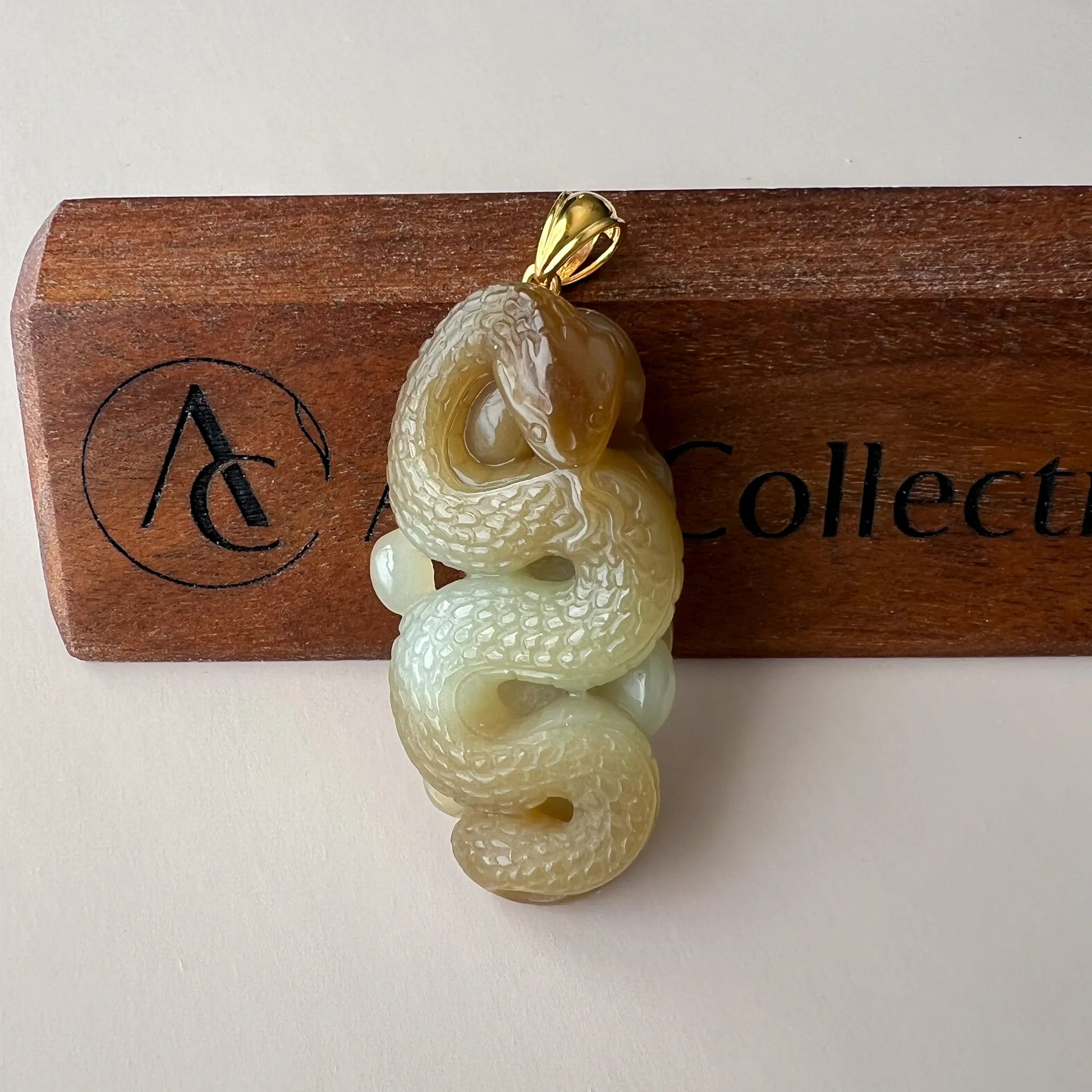 Front view of serpent pendant on branded wooden block, glossy carved jade with gold bail