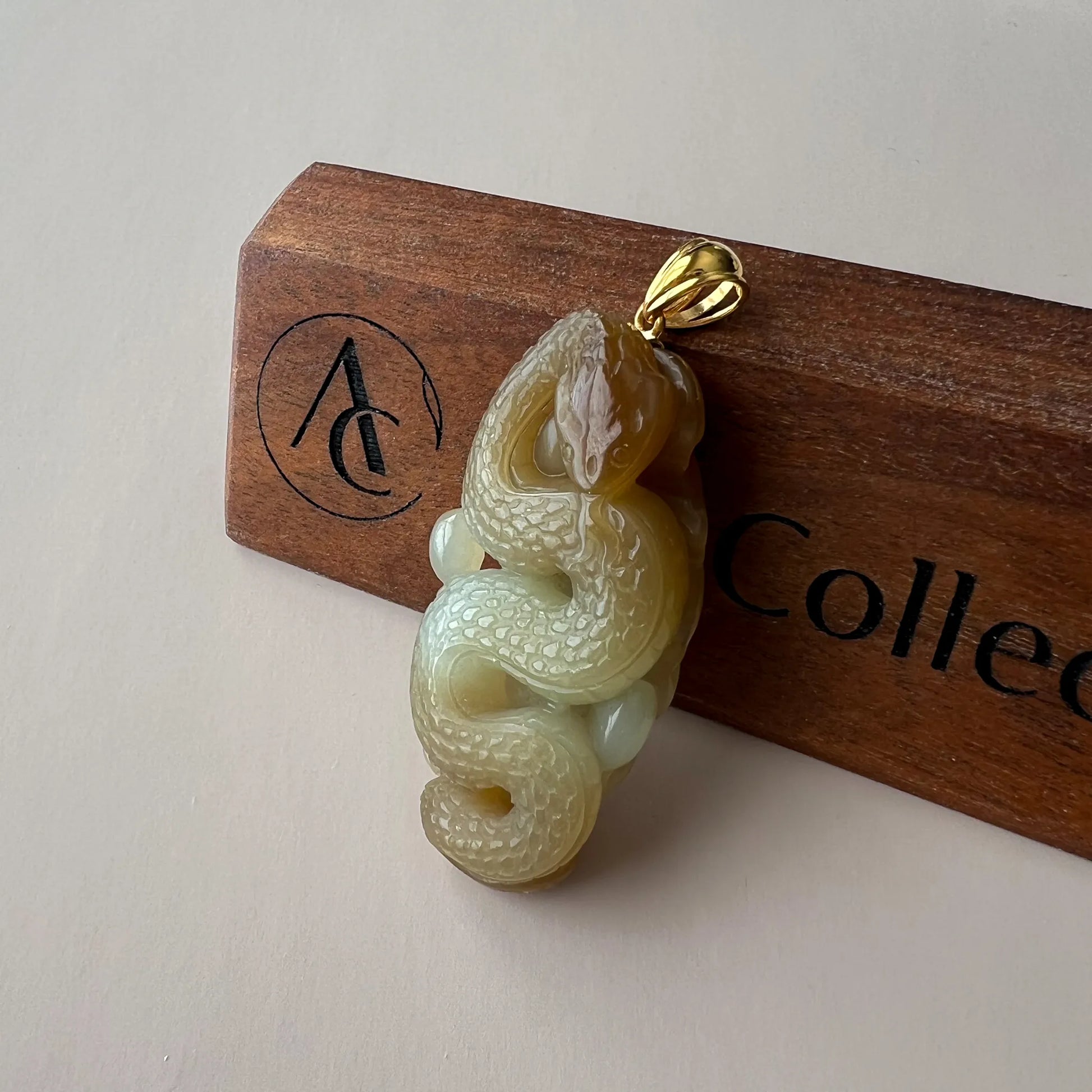 Hand-carved nephrite jade snake pendant with 18K gold bail, glossy textured finish, angled on wood display