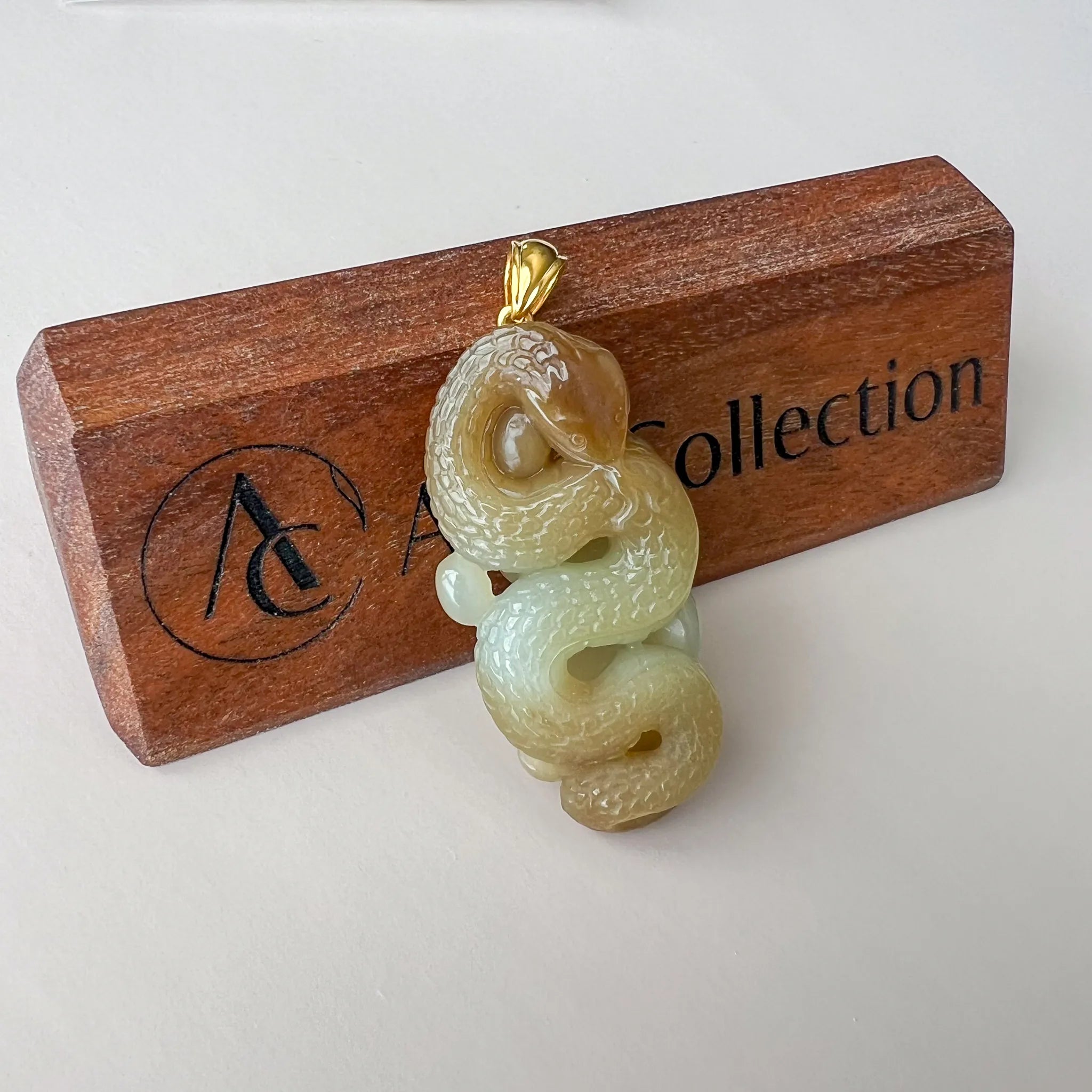 Front-facing pendant view on wooden block, detailed jade carving with polished gold bale