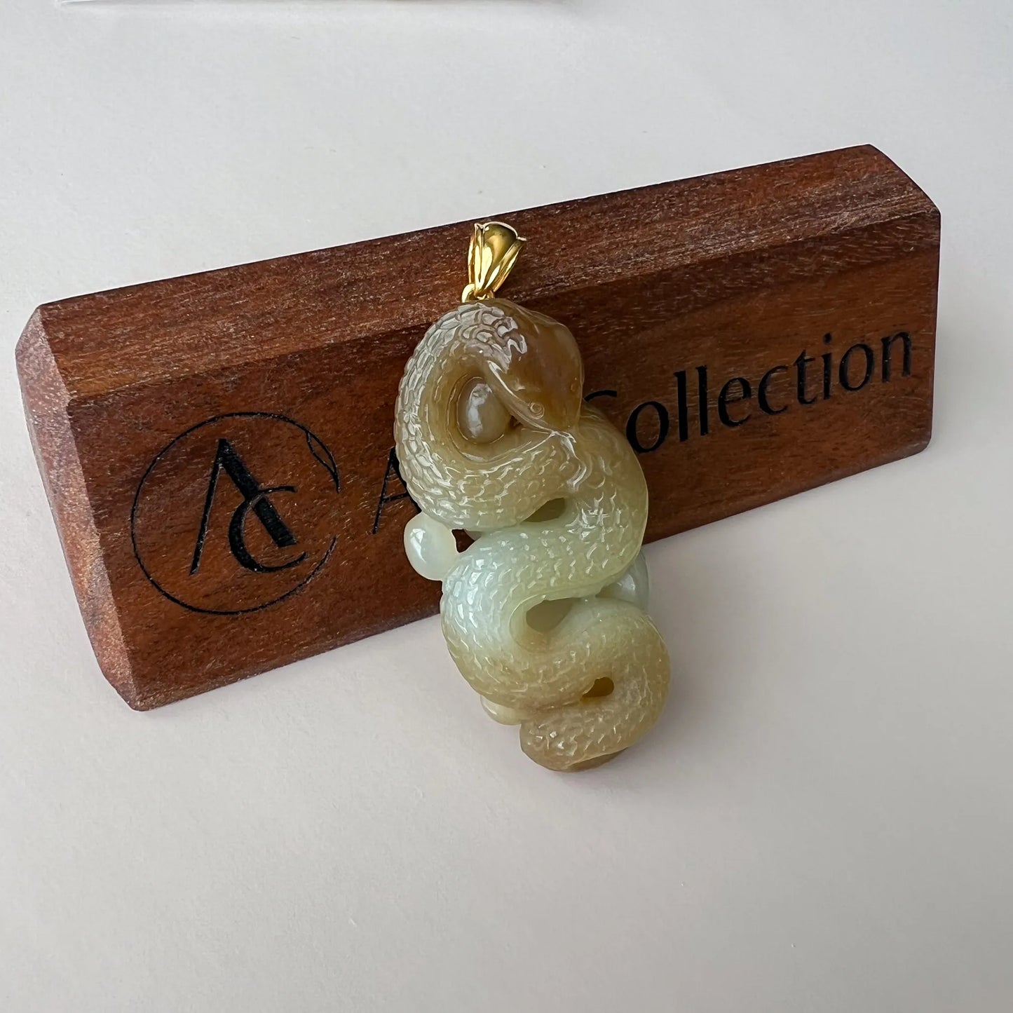 Front-facing pendant view on wooden block, detailed jade carving with polished gold bale