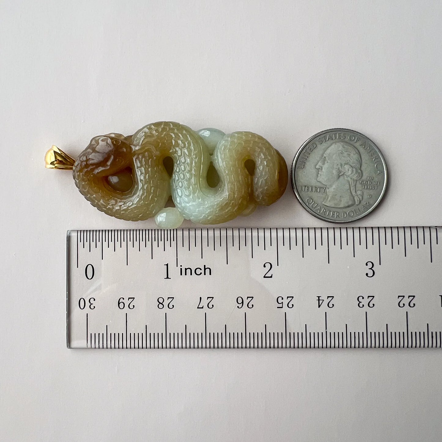 Side view of carved jade snake pendant beside ruler and quarter for scale, polished stone finish