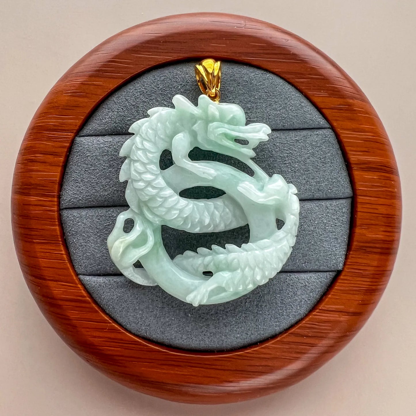 Front view of jade dragon pendant displayed in round wood case with gray padded insert