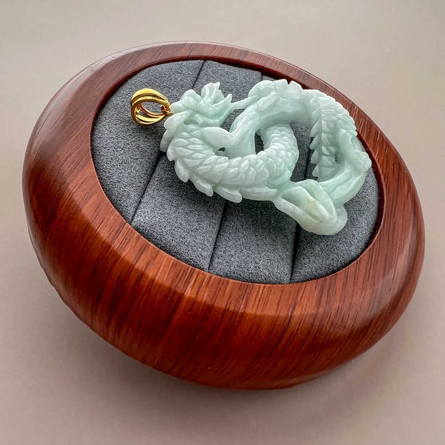 Angled side view of carved jade dragon pendant in round wood presentation box