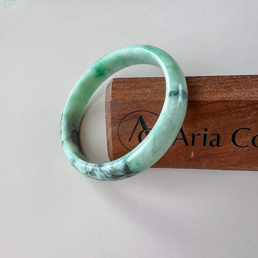 Green Burmese Type A jadeite jade bangle at an angle, polished glossy finish with mottled icy green and dark inclusions