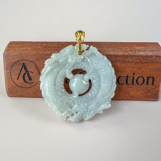 Light green gray jadeite twin dragons circle pendant with 18K gold bail, carved detail, front view on wood stand