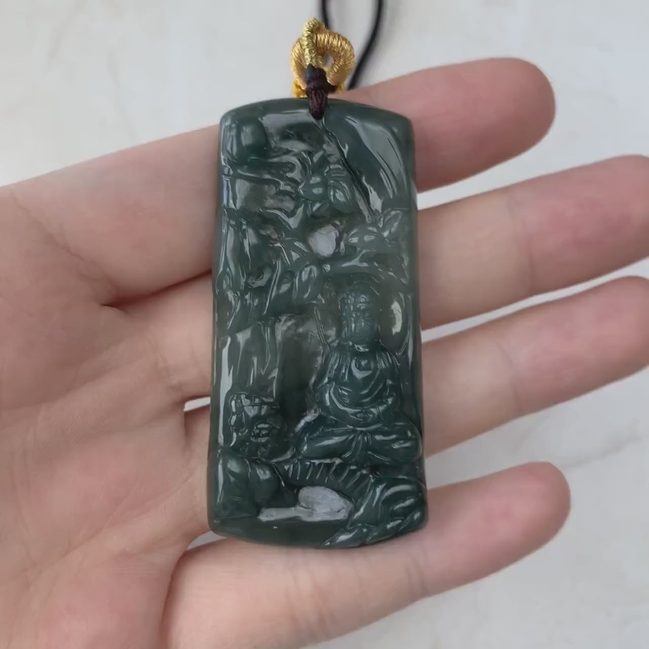 Video of a dark green semi-translucent jade pendant with intricate carved Buddha meditation scene and glowing finish