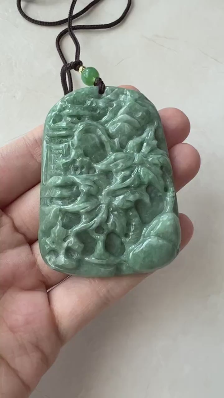 Video of hand-carved green jade pendant with tropical mountain, palm tree, and forest landscape design