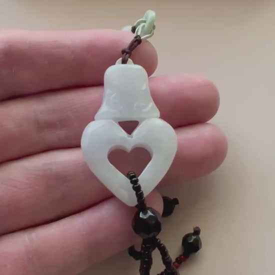 Video of an elegant pendant necklace with a heart-shaped design and ancient bell motif in polished metal, symbolic and gracef
