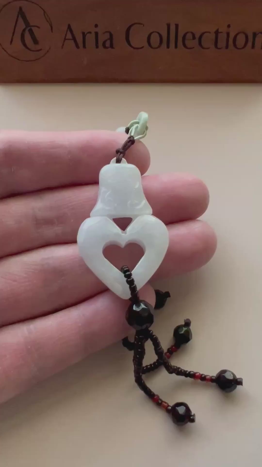 Video of an elegant pendant necklace with a heart-shaped design and ancient bell motif in polished metal, symbolic and gracef