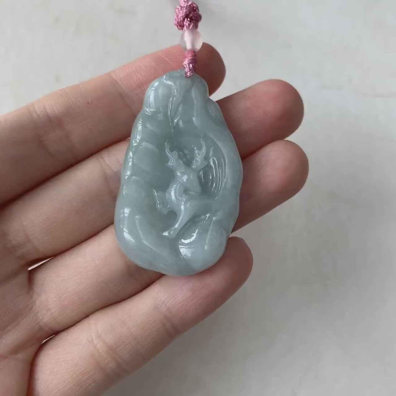 Video of a finely carved pendant depicting a deer in a forest scene with abstract mountain details, elegant and detailed.