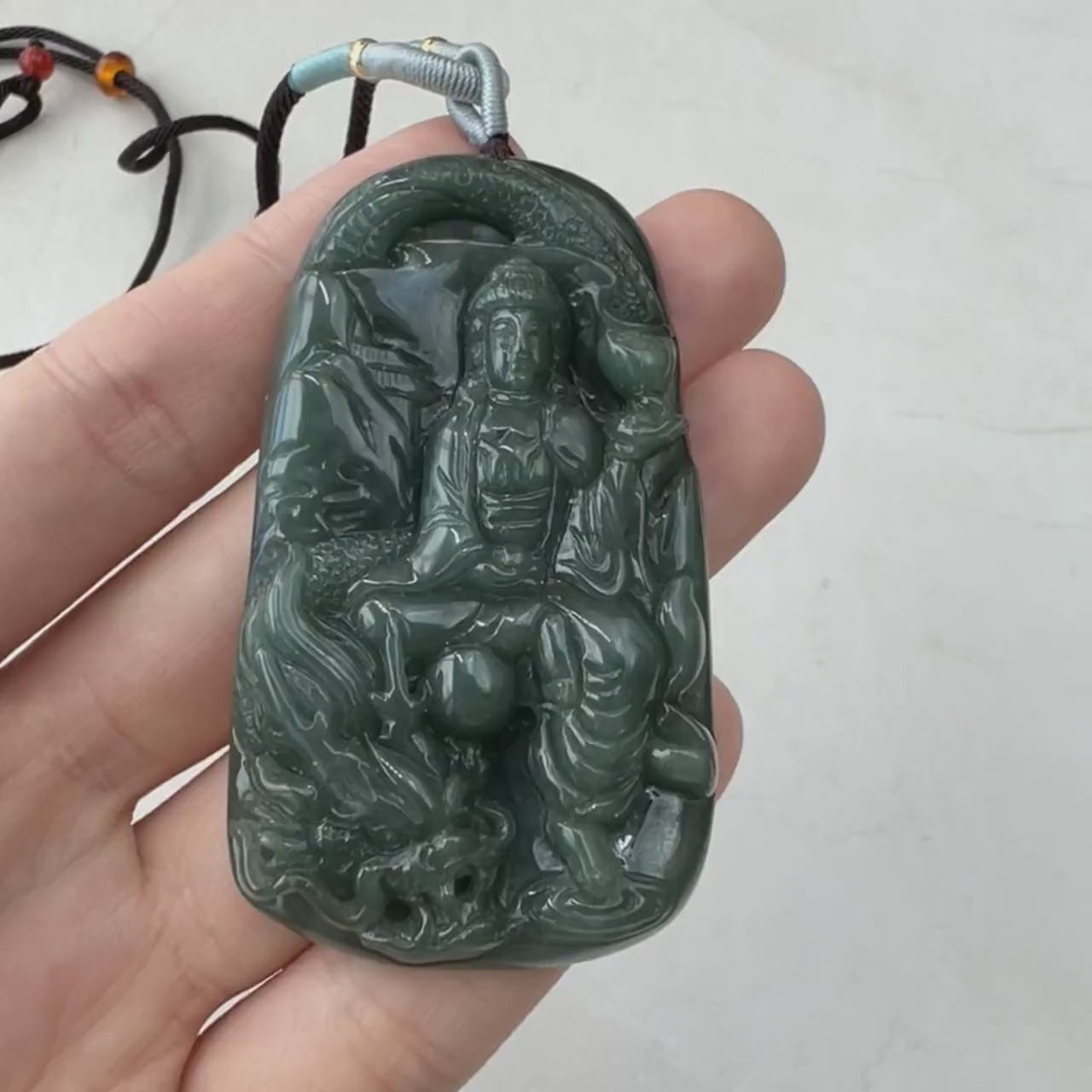 Video of a hand-carved natural jadeite Guan Yin pendant in rich dark green with intricate dragon details and a glowing semi-t