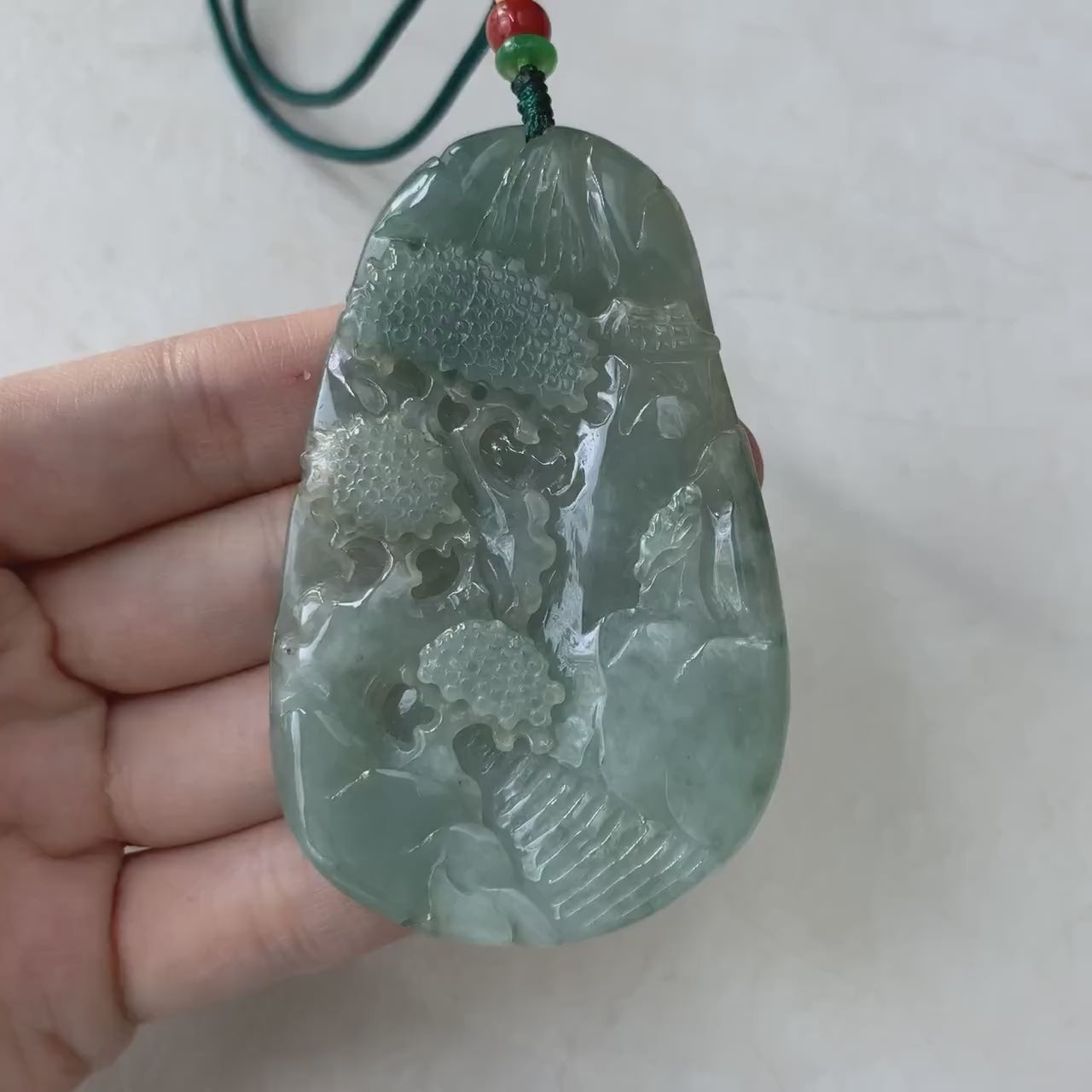 Video of a semi-translucent green jadeite pendant with hand-carved mountain forest landscape and intricate details