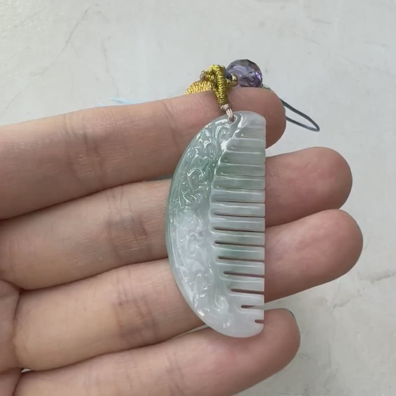 Video of a hand-carved light green semi-translucent natural jadeite comb charm with a smooth decorative finish