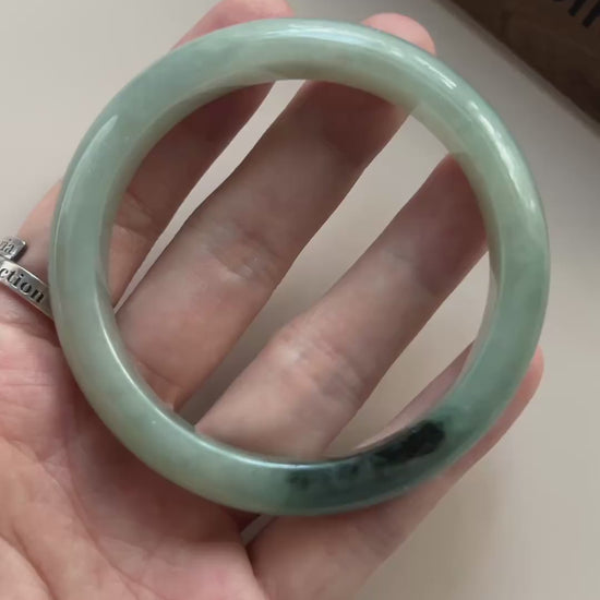 Video of a polished light green Burmese jadeite bangle with deep green-black natural color concentration and soft translucenc