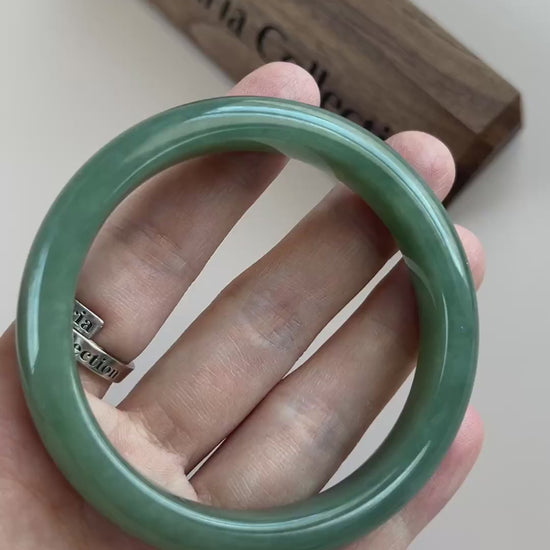 Video of a classic Burmese Type A jadeite bangle in rich green with mottled texture, polished rounded profile, and soft trans