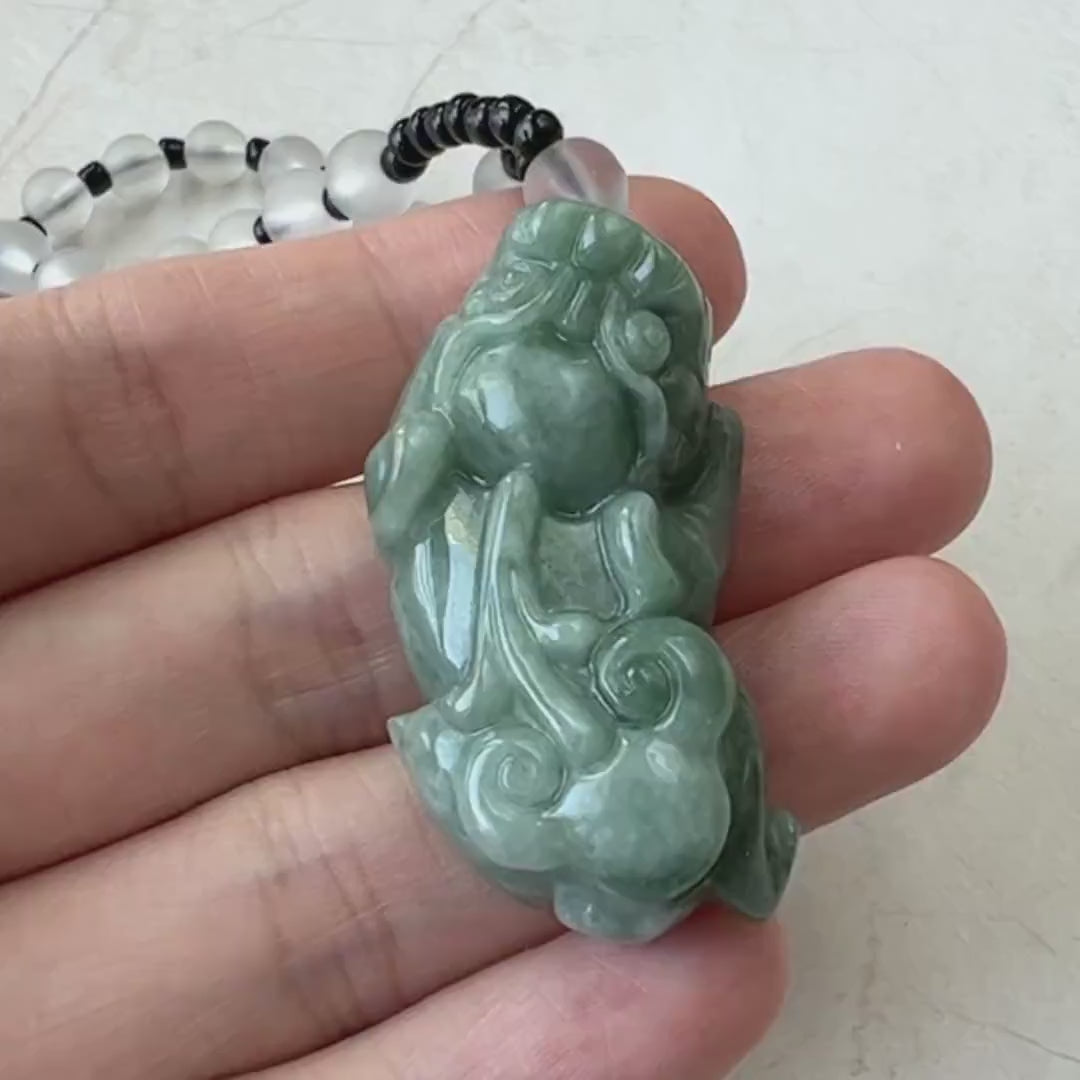 Video of a carved green jadeite Pi Xiu pendant on a natural albite stone necklace, glowing softly in light