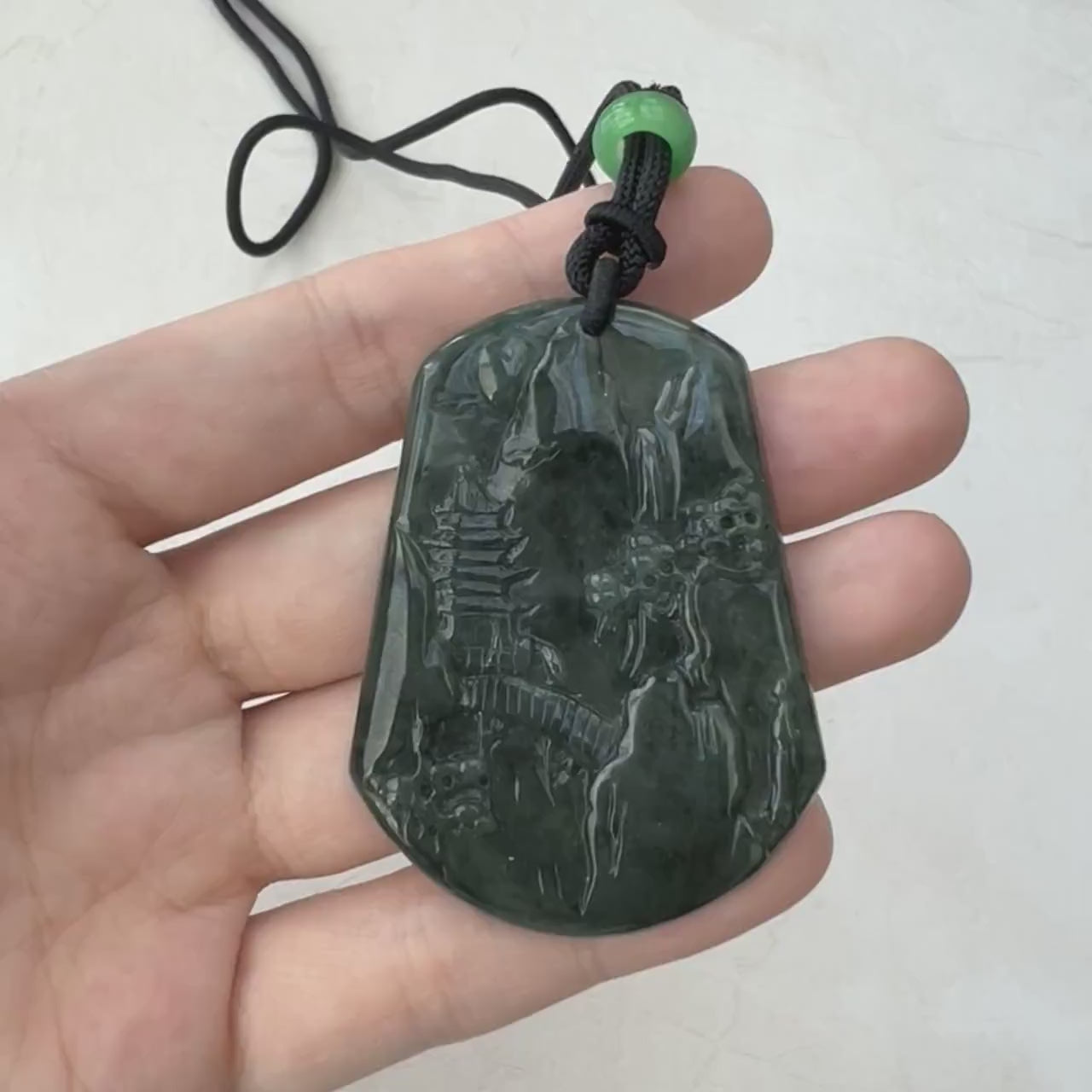 Video of a hand-carved dark green jade pendant with mountain forest landscape, semi-translucent and sculptural