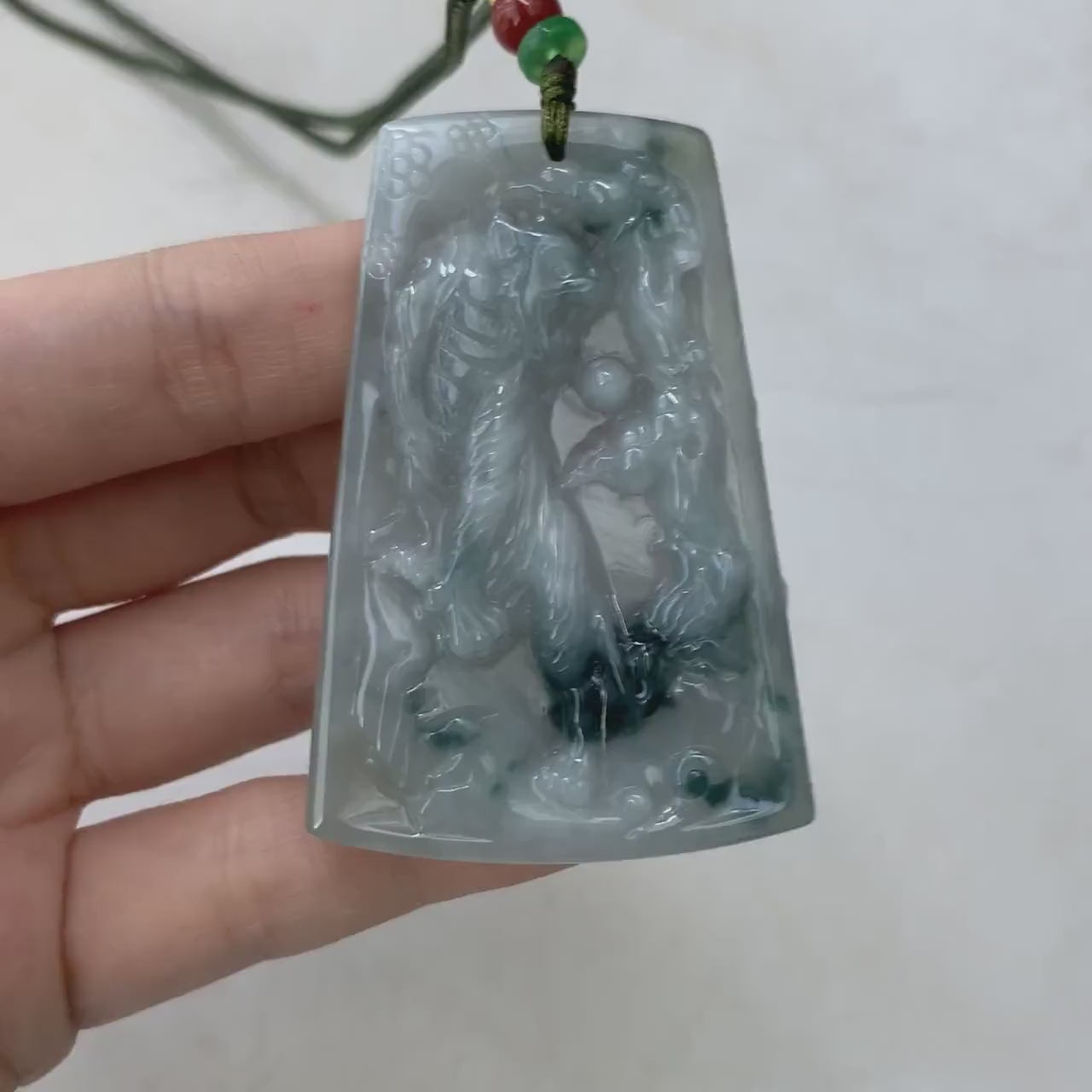 Video of a hand-carved green jade tiger pendant with detailed mountain scene and intricate fur texture