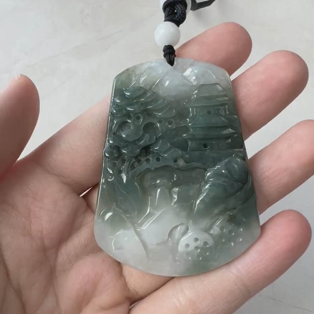 Video of hand-carved jadeite jade pendant in green, dark green and white with mountain landscape detail and soft glow