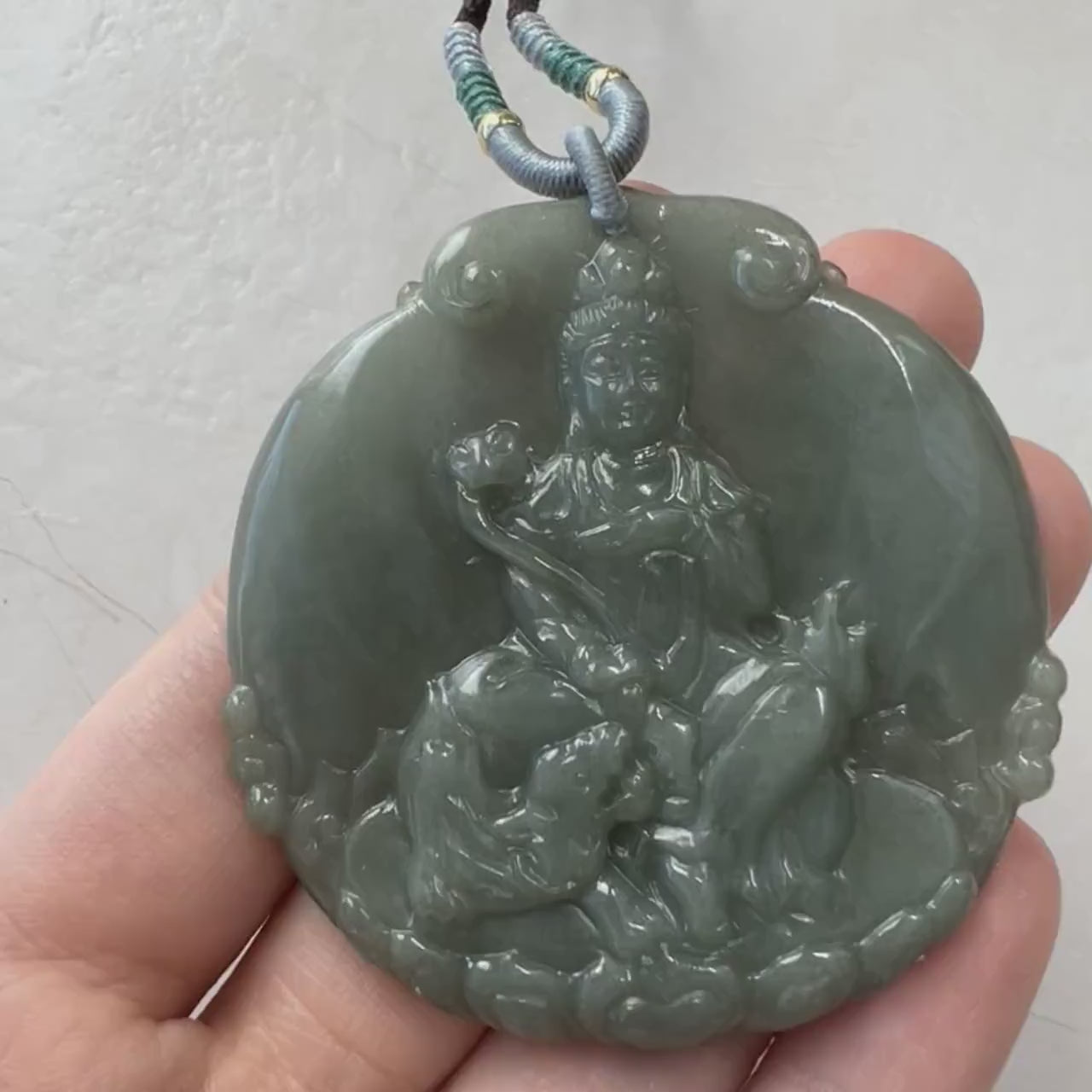 Video of a hand-carved green jade Guan Yin pendant in a meditative lotus pose with fine artisan detail
