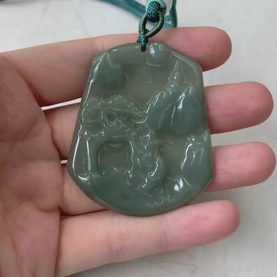 Video of a hand-carved dark olive green jade pendant with a serene mountain and forest landscape, semi-translucent glow