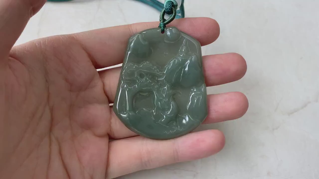Video of a hand-carved dark olive green jade pendant with a serene mountain and forest landscape, semi-translucent glow