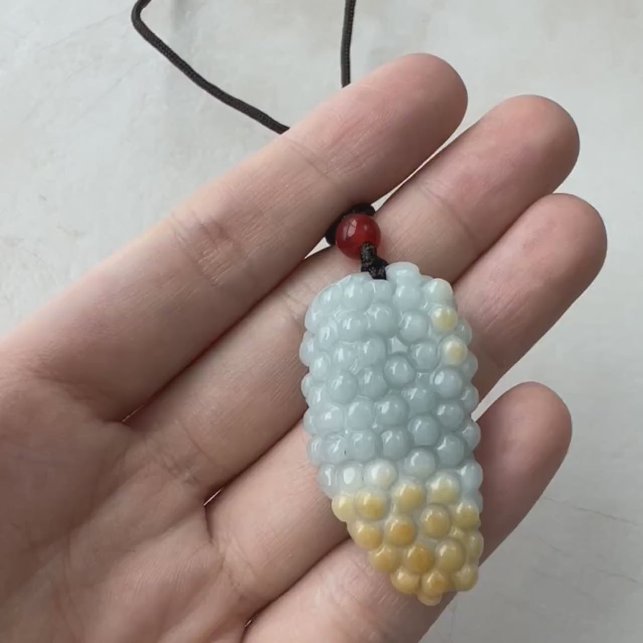 Video of hand-carved jade grape pendant in vibrant yellow tones with elegant minimalist design