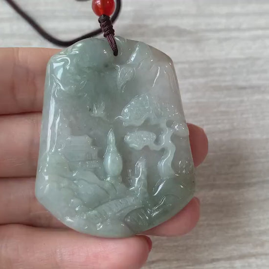 Video of a hand-carved green jade pendant with a serene mountain forest landscape, bridge, and tiny houses