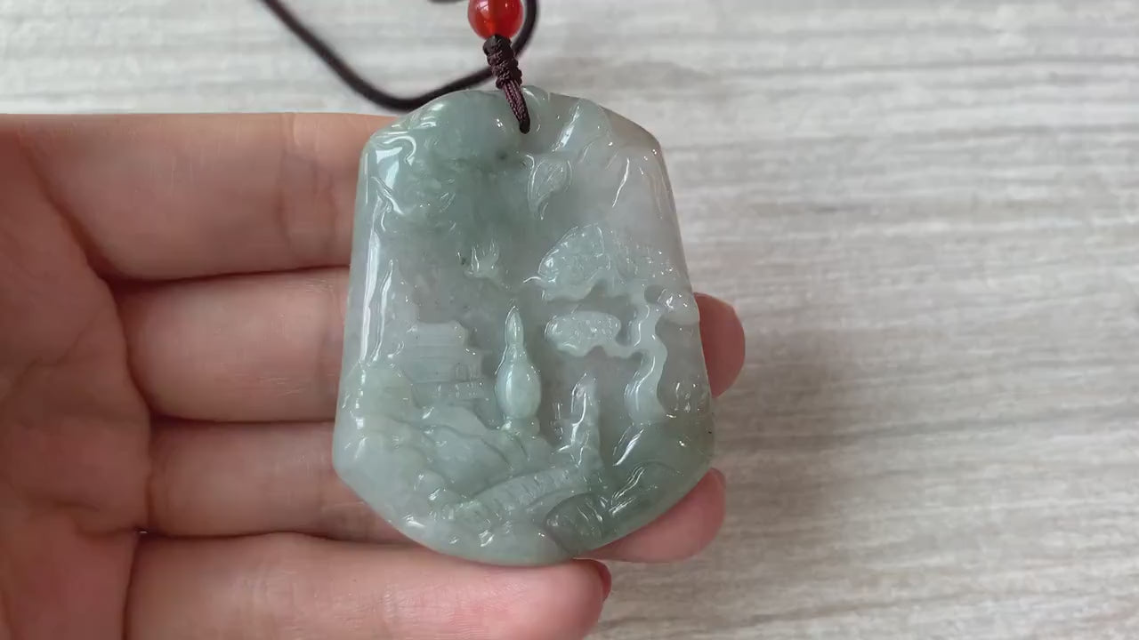 Video of a hand-carved green jade pendant with a serene mountain forest landscape, bridge, and tiny houses