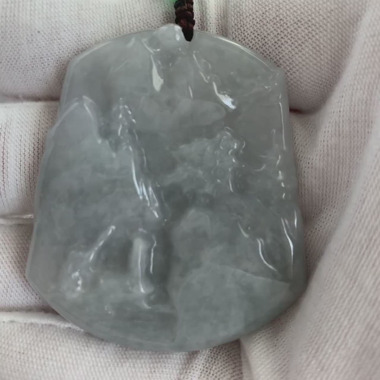Video of a hand-carved jade pendant in green with an abstract moonlit mountain and forest landscape design