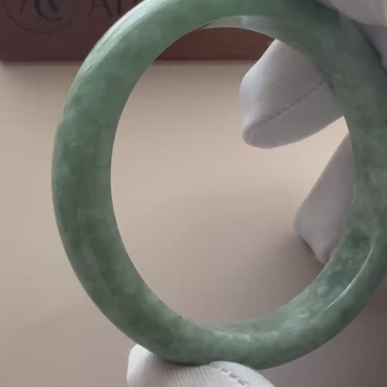 Video of a polished Burmese jadeite bangle in mottled light and medium green with a classic smooth profile