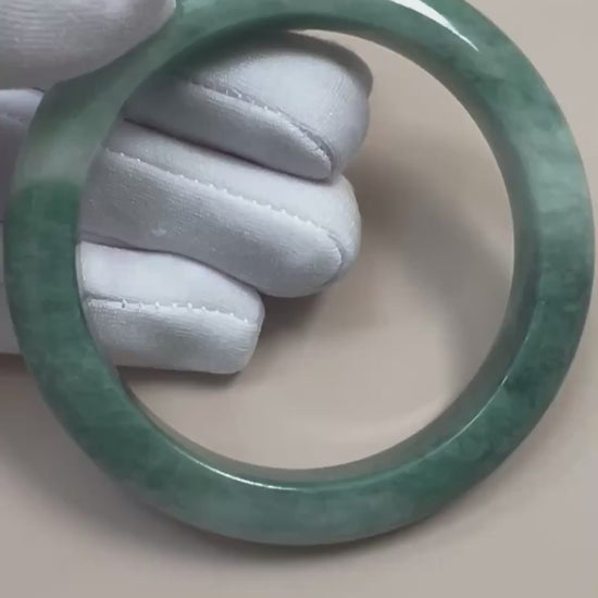 Video of a polished Burmese Type A jadeite bangle with layered green tones, mottled texture, and rounded profile