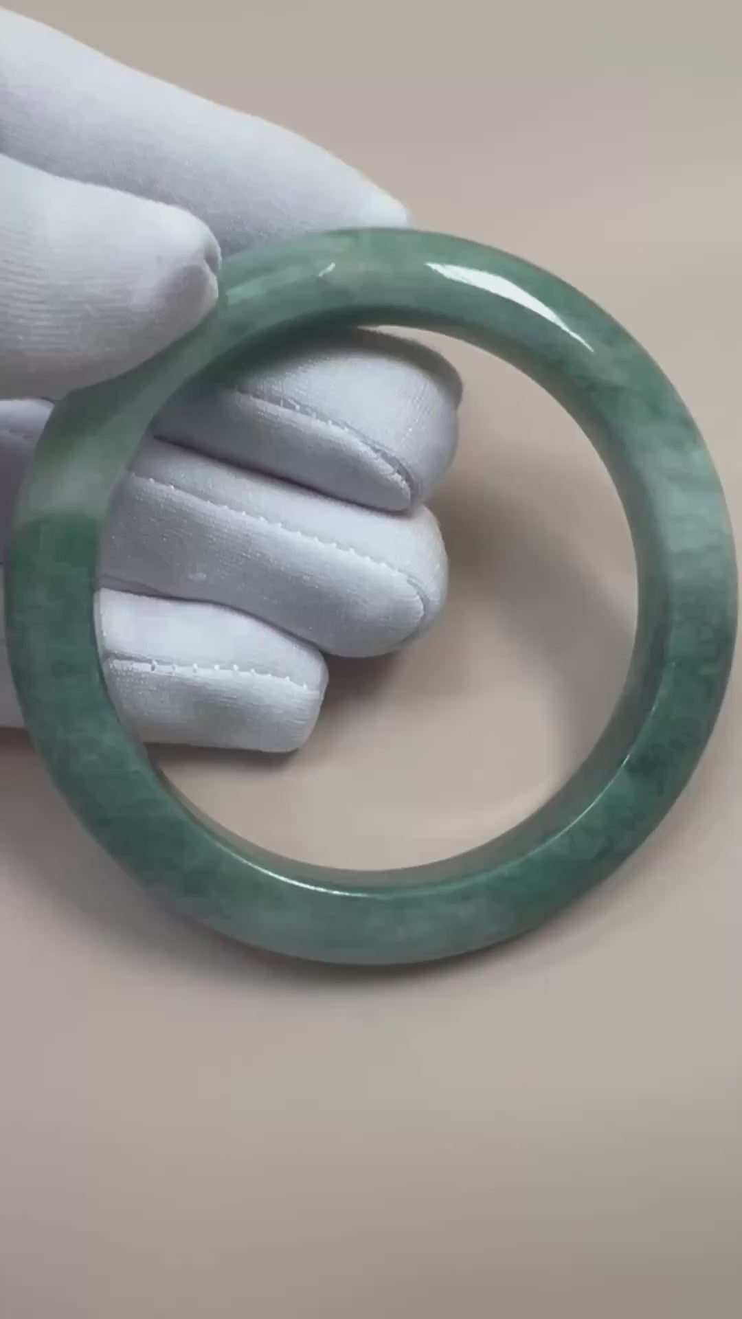 Video of a polished Burmese Type A jadeite bangle with layered green tones, mottled texture, and rounded profile