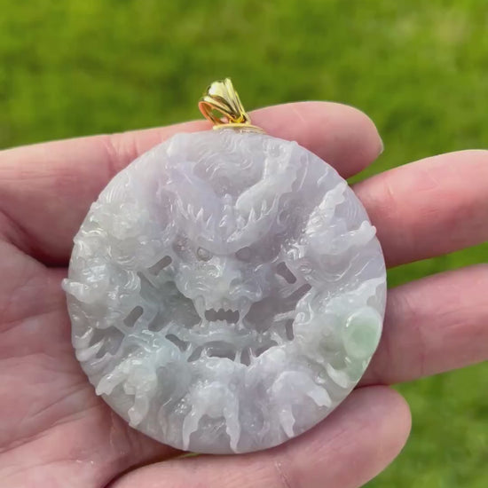 Video of a hand holding a round carved jade pendant with a dragon design, featuring a gold-colored bail, set against a blurred green grass background.