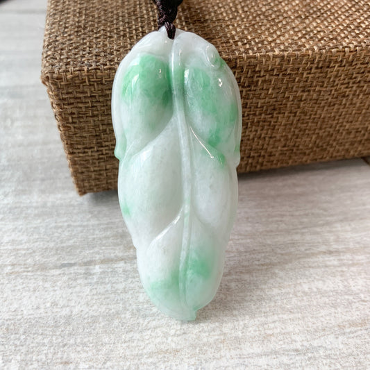 Close-up of hand-carved jade leaf pendant, white and green polished stone on dark cord, front view
