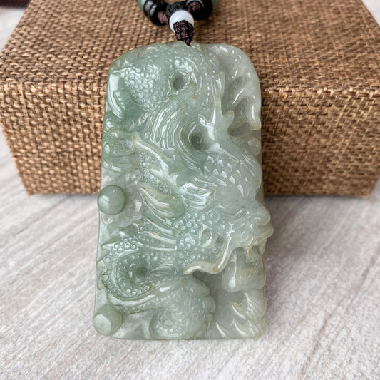 Close-up of pale green jadeite jade dragon pendant necklace, hand-carved with glossy polished texture and cord loop