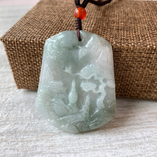 Close-up of hand-carved pale green jadeite pendant with mountain forest river relief, glossy finish, on cord necklace