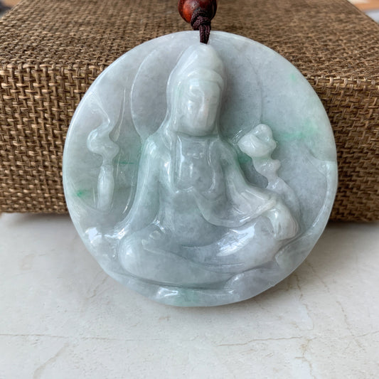 Hand-carved pale jadeite Guan Yin pendant necklace, glossy translucent finish, front view on woven mat background