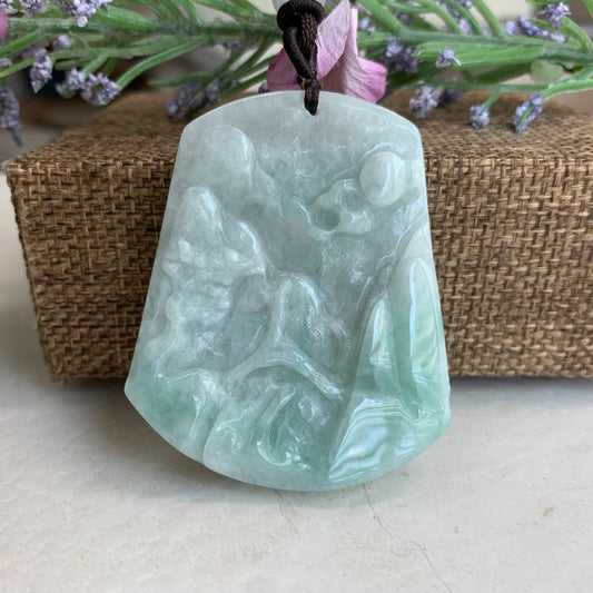 Close-up of pale green jadeite pendant with hand-carved landscape scene, glossy finish, front view on cord
