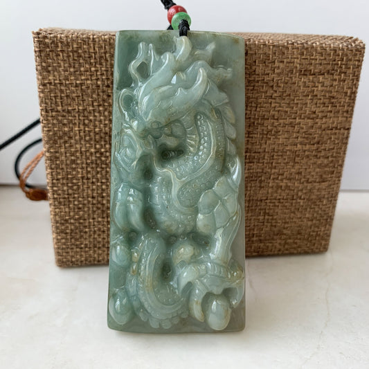 Close-up of large green jade dragon pendant necklace, hand-carved glossy jadeite with textured relief on cord display