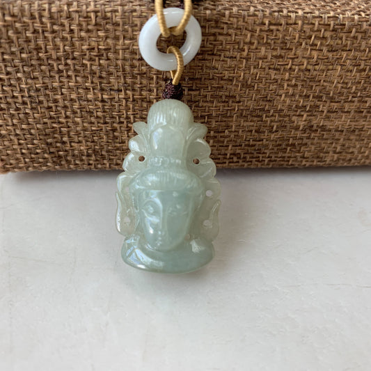 Close-up of translucent jade Guan Yin pendant with carved face, hanging on cord against woven background