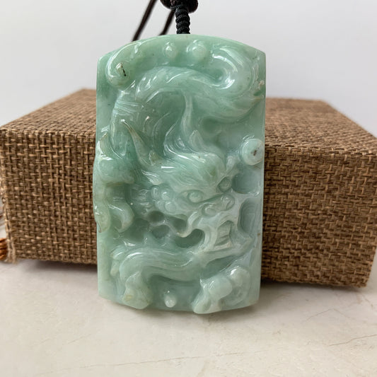 Close-up front view of a pale green jadeite dragon pendant with glossy hand-carved texture on a black cord